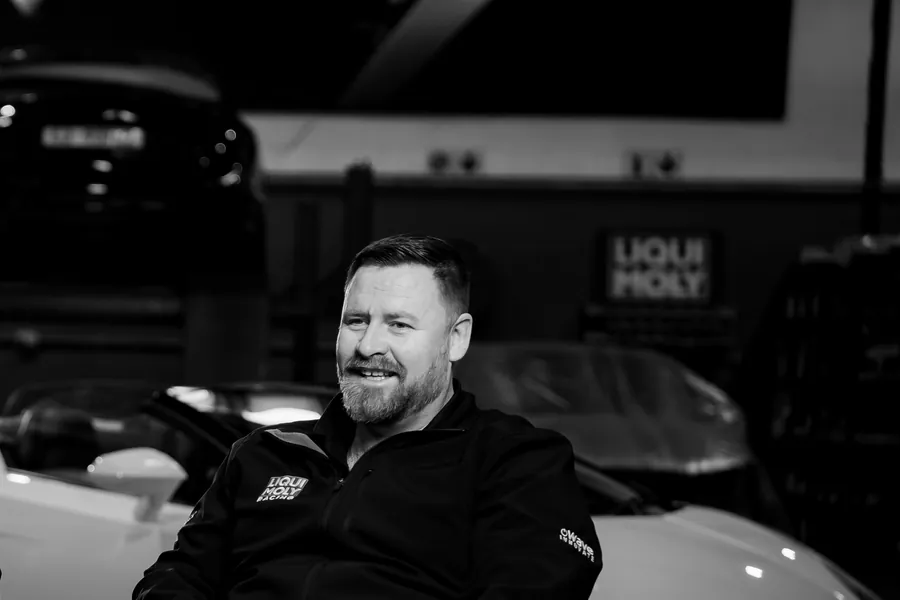 A member of the Tuned 2 Race team smiling in the workshop, black and white