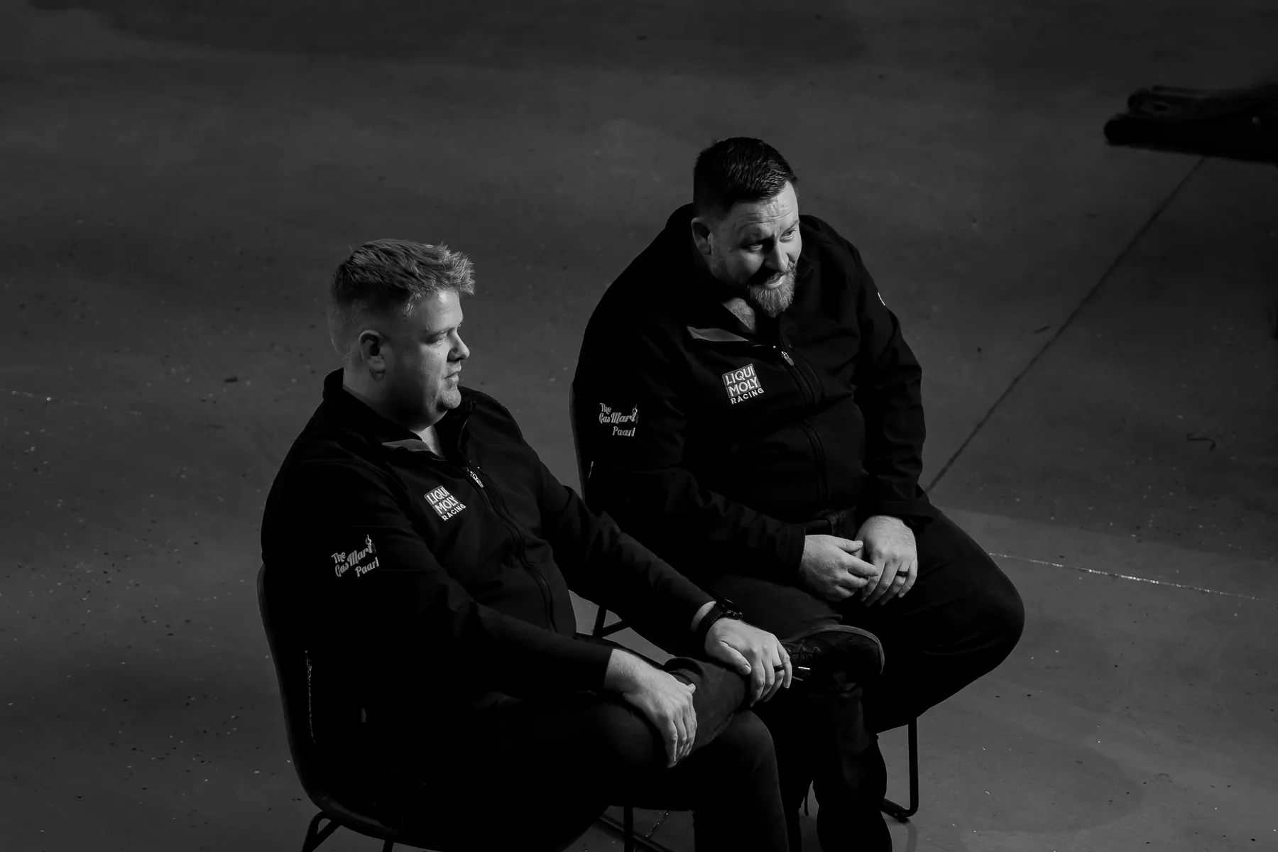 Two members of the Tuned 2 Race team sharing a laugh in the workshop, black and white